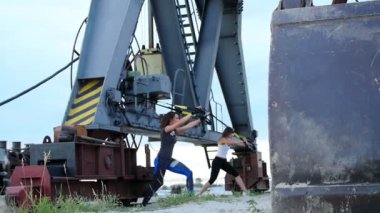 Şafakta kargo vinç, iki genç güzel, atletik kızlar süspansiyon askıları trx ile egzersiz yaparak yakınındaki. Tüm vücut kas çalışması için fitness egzersizleri.