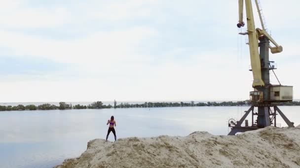 운동 선수인 젊은 여성 복싱은 채 석장의 모래 위에서 야외에서 운동을 했습니다. 뒤에서는 강, 화물선, 새벽을 볼 수있다. 에어로 비디오 촬영 — 비디오