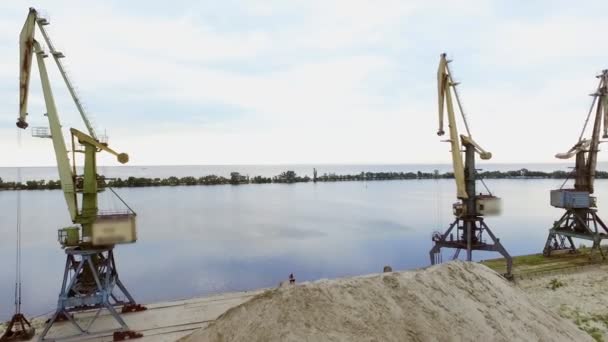 Młoda, wysportowana kobieta ćwiczy, Squats, na piaszczystym szczycie kamieniołomu, na plaży. Na tle widać rzekę, dźwigi towarowe, świt. Zdjęcia wideo z lotu ptaka — Wideo stockowe