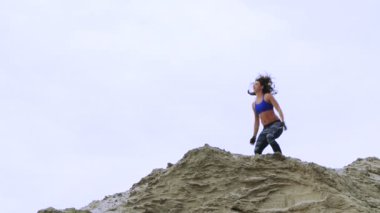 young, athletic woman in a Blue top and striped leggens doing exercises, Squats, on the sandy top of the quarry, fitness At sunrise, on the beach in a cargo port.