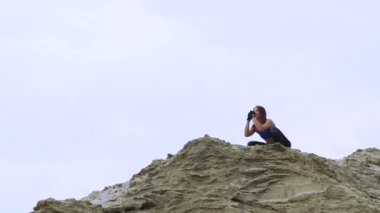 young, athletic woman in a Blue top and striped leggens doing exercises, Squats, on the sandy top of the quarry, fitness At sunrise, on the beach in a cargo port.