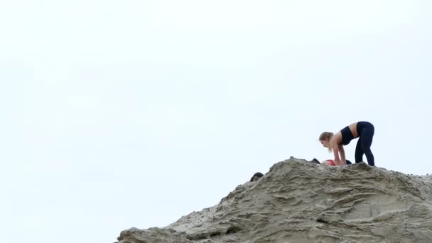 Três mulheres jovens e atléticas fazendo exercícios de alongamento, aquecimento, no topo arenoso da pedreira, na praia. amanhecer . — Vídeo de Stock