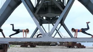 İki kadın, genç, atletik güç egzersizleri yapın. Bir yük vinç metal kiriş üzerinde duruyorlar. bir kargo liman plajında şafak, Fitness.