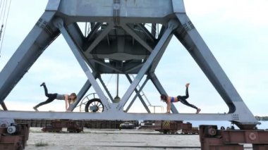 İki kadın, genç, atletik güç egzersizleri yapın. Bir yük vinç metal kiriş üzerinde duruyorlar. bir kargo liman plajında şafak, Fitness.