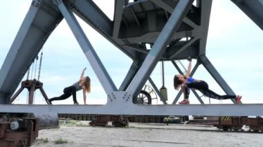 İki kadın, genç, atletik güç egzersizleri yapın. Bir yük vinç metal kiriş üzerinde duruyorlar. bir kargo liman plajında şafak, Fitness.