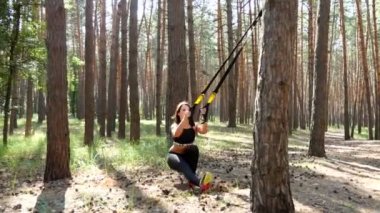 Güzel, atletik, seksi genç kadın, Koç, eğitmen, egzersiz, fitness trx sistemi, Trx askı kayışları ile egzersizleri yapıyor gerçekleştirir. Çam ormanı içinde yaz, güneş ışınları.