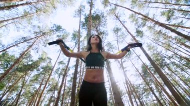 atletik kadın, Koç, eğitmen, gerçekleştirir, fitness trx sistemi, Trx askı kayışları ile yapıyor. Çam ormanı içinde yaz, güneş ışınları. Aşağıdan görüntülemek için Görünüm alt