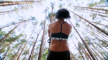 atletik kadın, Koç, eğitmen, gerçekleştirir, fitness trx sistemi, Trx askı kayışları ile yapıyor. Çam ormanı içinde yaz, güneş ışınları. Aşağıdan görüntülemek, arkadan görünüm