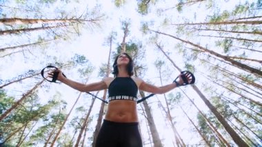 atletik kadın, Koç, eğitmen, gerçekleştirir, fitness trx sistemi, Trx askı kayışları ile yapıyor. Çam ormanı içinde yaz, güneş ışınları. Aşağıdan görüntülemek için Görünüm alt