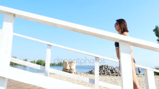 Mujer joven hermosa, atlética, sexy, en gafas de sol, en traje de baño, entrenador, instructor, realiza ejercicios. En la playa, cerca del mar, río, en verano, en los rayos del sol . — Vídeo de stock