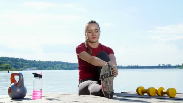 Мбаппе, атлетичная молодая женщина, тренер, инструменталист, растягивающийся, делающий разные упражнения. Озеро, река, голубое небо и лес на заднем плане, летний солнечный день — стоковое видео