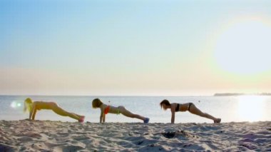 zaman uyumlu olarak şınav, egzersizleri yapıyor üç güzel, atletik kadınlar, mayo. Kumsalda, yaz, günbatımı, güneş ışınları.