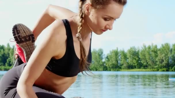 Hermosa, atlética joven rubia, entrenador, instructor, estiramiento, haciendo diferentes ejercicios. Lago, río, cielo azul y bosque en el fondo, día soleado de verano. primer plano — Vídeo de stock