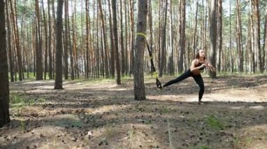 Güzel, atletik, seksi genç kadın, Koç, eğitmen, egzersiz, fitness trx sistemi, Trx askı kayışları ile egzersizleri yapıyor gerçekleştirir. Çam ormanı içinde yaz, güneş ışınları.