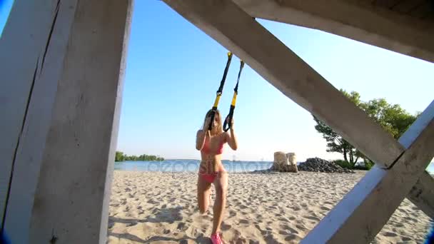 Tre atletisk, sexiga unga kvinnor i baddräkter, instruktörer, gör övningar med fitness trx system, Trx suspension remmar. På stranden i sommar, vid solnedgång, i solens strålar. — Stockvideo