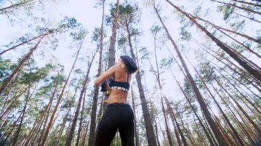 atletik kadın, Koç, eğitmen, gerçekleştirir, fitness trx sistemi, Trx askı kayışları ile yapıyor. Çam ormanı içinde yaz, güneş ışınları. Aşağıdan görüntülemek, arkadan görünüm