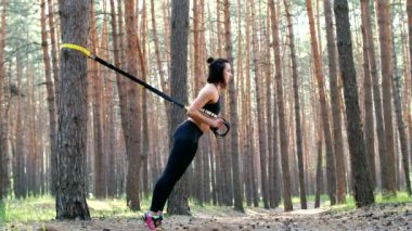 Güzel, atletik, seksi genç kadın, Koç, eğitmen, egzersiz, fitness trx sistemi, Trx askı kayışları ile egzersizleri yapıyor gerçekleştirir. Çam ormanı içinde yaz, güneş ışınları.