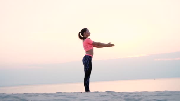 Mulher bonita saudável, jovem meditando, praticando ioga entre a areia, na praia, junto ao mar, rio, ao amanhecer, ao nascer do sol, close-up — Vídeo de Stock