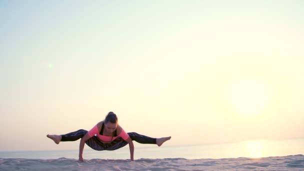 Sănătoasă, tânără femeie frumoasă meditând, întinzându-se, practicând yoga pe plaja mării, la răsăritul soarelui, face exerciții pentru echilibru și coordonare, tonus muscular profund . — Videoclip de stoc