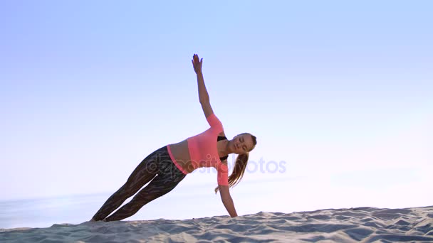 Mujer joven y saludable haciendo ejercicios para músculos oblicuos de la presión abdominal,, en la playa, al amanecer, hace ejercicios para el equilibrio y la coordinación, tono muscular profundo . — Vídeos de Stock