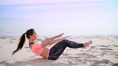 Sağlıklı, genç güzel kadın egzersiz kasları basına alır vücut, bacak, pompalar için sahilde kum güneş doğarken yatan basın gerçekleştirir