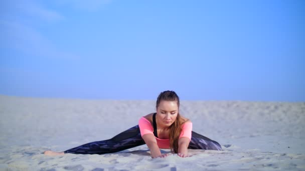 Здорова, молода красива жінка, що розтягується, практикує йогу на пляжі, під час сходу сонця, робить вправи для рівноваги та координації, тонус глибоких м'язів. розслаблення м'язів, розум — стокове відео