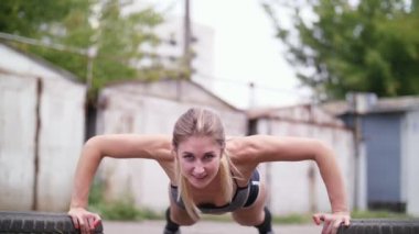 seksi atletik genç sarışın kadın şort, eski terk edilmiş garajlar yakınındaki yaz aylarında lastikler, şınav, yardımıyla çeşitli güç egzersizleri gerçekleştirir