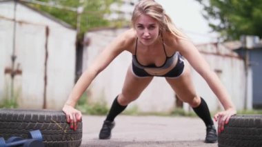 seksi atletik genç sarışın kadın şort, eski terk edilmiş garajlar yakınındaki yaz aylarında lastikler, şınav, yardımıyla çeşitli güç egzersizleri gerçekleştirir