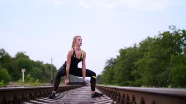 Güzel seksi atletik genç sarışın kadın siyah tozluk yaz aylarında demiryoluna raylar, traversler egzersizleri bir ağır ağırlık plaka ile performans. Ağır çekim