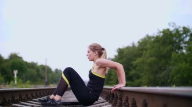 Güçlü kol kasları, yapmak için güzel seksi atletik genç sarışın kadın çalışmaları gerçekleştirme siyah tozluk presler ellerinde. Yaz aylarında uyuyanlar, bir demiryolu üzerinde oturur