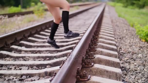 Primo piano, gambe atletiche femminili in scarpe da ginnastica nere e leggings saltano sulla rotaia, sulla ferrovia, in estate. femmina esegue esercizi per le gambe , — Video Stock