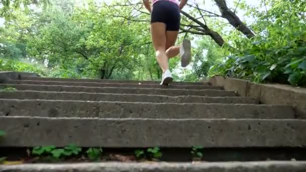 Beautiful sexy athletic young blond woman in a T-shirt and shorts, runs upstairs, in the forest, park, in summer day. Bottom view, from the back. Slow motion — Stock Video