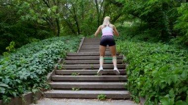 Güzel seksi atletik genç sarışın kadın üst katta, ormanda, park, yaz günü içinde çalışır. Bacak merdivenlerde farklı kasları güçlendirmek için egzersizler gerçekleştirir.