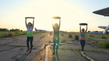 güneş gözlüğü, tayt, ağırlığı, egzersizleri yapıyor gün batımı, atletik, genç kadınlarda, ağır ağırlık plaka, terkedilmiş bir Havaalanı, eski bir uçak arka planı üzerinde,