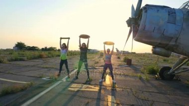 güneş gözlüğü, tayt, ağırlığı, egzersizleri yapıyor gün batımı, atletik, genç kadınlarda, ağır ağırlık plaka, terkedilmiş bir Havaalanı, eski bir uçak arka planı üzerinde,