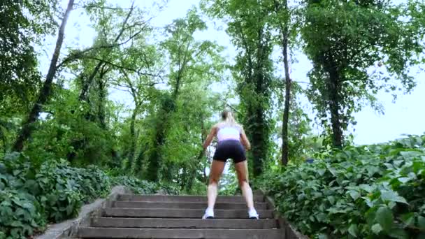 Beautiful sexy athletic young blond woman runs upstairs, in the forest, park, in summer day. Performs exercises to strengthen the different muscles of the legs on the stairs. — Stock Video