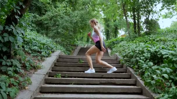 Bella sexy atletica giovane donna bionda corre di sopra, nella foresta, parco, nella giornata estiva. Esegue esercizi per rafforzare i diversi muscoli delle gambe sulle scale . — Video Stock