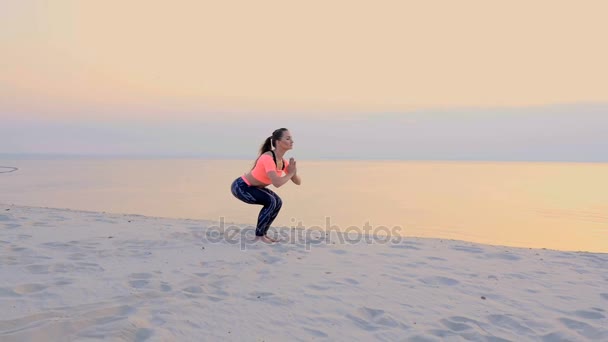 Здоровая, молодая красивая женщина медитирует, растягивает, практикует йогу на морском пляже, на восходе солнца, делает упражнения для равновесия и координации, глубокий мышечный тонус . — стоковое видео