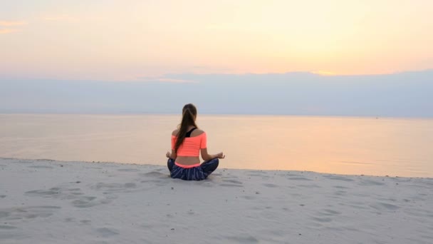 Mulher bonita saudável, jovem meditando, praticando ioga na praia, junto ao mar, ao nascer do sol, relaxa os músculos, mente, adquire a harmonia da alma e do corpo — Vídeo de Stock