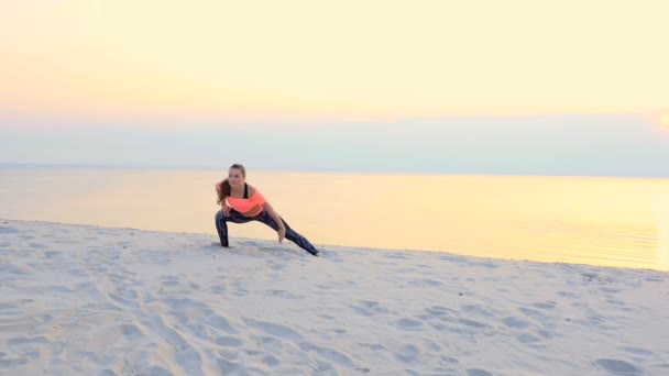 Mulher bonita saudável, jovem meditando, alongamento, praticando ioga na praia do mar, ao nascer do sol, faz exercícios de equilíbrio e coordenação, tônus muscular profundo — Vídeo de Stock