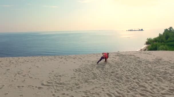 Mulher bonita saudável, jovem em óculos de sol meditando, alongamento, praticando ioga na praia do mar, ao nascer do sol, Faz exercícios de equilíbrio, coordenação, tom muscular profundo . — Vídeo de Stock