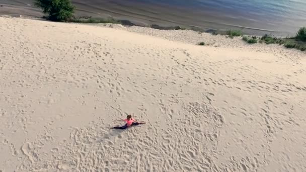 Mujer joven y saludable en gafas de sol meditando, estirando, practicando yoga en la playa del mar, al amanecer, hace ejercicios para el equilibrio, coordinación, tono muscular profundo . — Vídeos de Stock