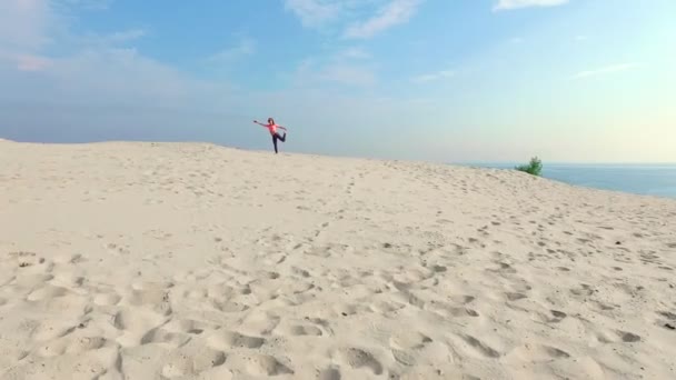 Mujer joven y saludable en gafas de sol meditando, estirando, practicando yoga en la playa del mar, al amanecer, hace ejercicios para el equilibrio, coordinación, tono muscular profundo . — Vídeos de Stock