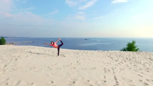 Donna sana, giovane e bella con gli occhiali da sole che medita, si allunga, pratica yoga sulla spiaggia, all'alba, fa esercizi per l'equilibrio, la coordinazione, il tono muscolare profondo . — Video Stock