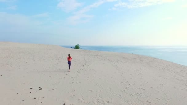 Здоровая, молодая спортивная красивая женщина в солнечных очках бежит по песку, на пляже, летом, к солнцу, на восходе солнца. Авиационные съёмки — стоковое видео