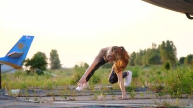Güzel, atletik, genç kadın güneş gözlüğü, tayt, farklı güç egzersizleri, atlar, şınav, bacaklar kaldırma gerçekleştirir. bir terk edilmiş Havaalanı, eski uçak yakınındaki