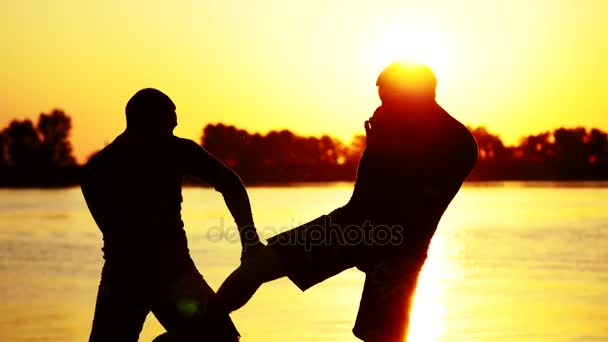 Zwei dunkle männliche Figuren, bei Sonnenaufgang, gegen das Licht, Boxen, Kämpfen im Sparring, Training in zwei Schlagtechniken. am Sandstrand, im Frachthafen, am Wasser, im Sommer — Stockvideo