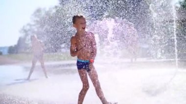 yedi yaşında eğleniyor arasında su jetleri, Çeşme, etrafta çocuk heyecanlı, serpin, iyi eğlenceler, iyi eğlenceler, sıcak yaz gününde. Şehirde yaz. Ağır çekim