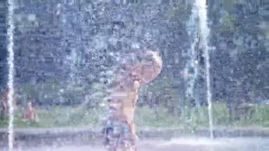 yedi yaşında eğleniyor arasında su jetleri, Çeşme, etrafta çocuk heyecanlı, serpin, iyi eğlenceler, iyi eğlenceler, sıcak yaz gününde. Şehirde yaz. Ağır çekim