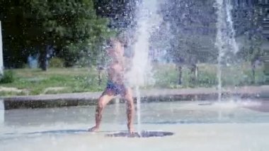 yedi yaşında eğleniyor arasında su jetleri, Çeşme, etrafta çocuk heyecanlı, serpin, iyi eğlenceler, iyi eğlenceler, sıcak yaz gününde. Şehirde yaz. Ağır çekim